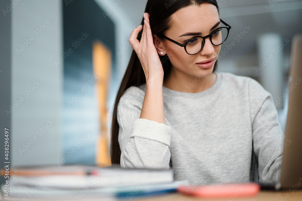Brunette focused young woman in eyeglasses working with laptop at home Brunette focused young woman in eyeglasses working with laptop at home