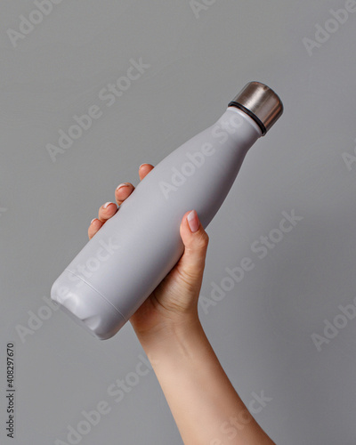 Hand with grey rinsulated bottle on grey background