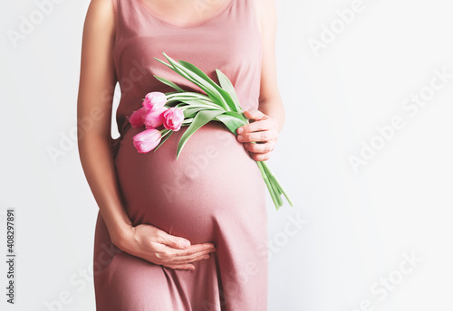 Fototapeta Beautiful pregnant woman with tulips flowers holds hands on belly