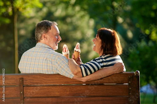 Retired couple on the park bench eating ice-cream. Loving mature man and woman sits outdoors.