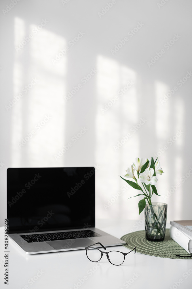 Workplace, home desk with laptop computer, glasses and notebook lying on white desk with a beautiful spring flower at background. Workplace, home desk with laptop computer, glasses and notebook lying on white desk with a beautiful spring flower at background.