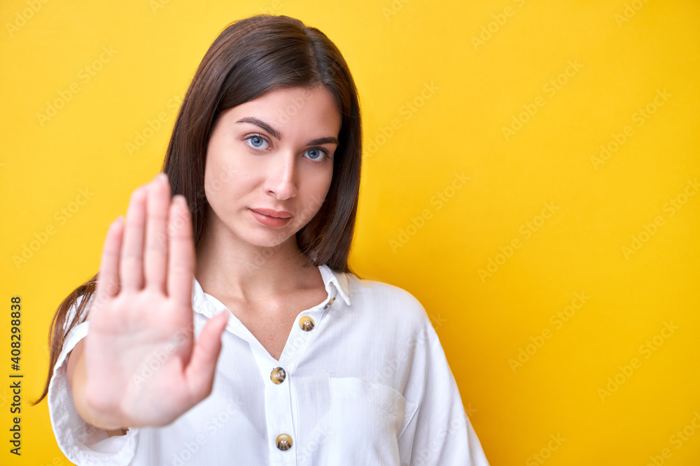 Brunette girl showing stop gesture with hands, looking at the camera with strong face isolated on yellow background, keep distance Brunette girl showing stop gesture with hands, looking at the camera with strong face isolated on yellow background, keep distance