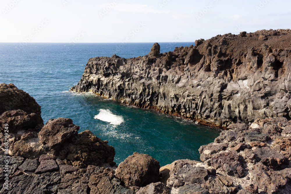 Volcanic coastline by the sea in Los Hervideros tourist attraction in Lanzarote island. Blue ocean water splashing over black rocks cliffs