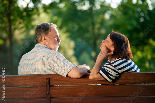 Back view retired couple fooling around on the bench. Man and woman making funny faces.