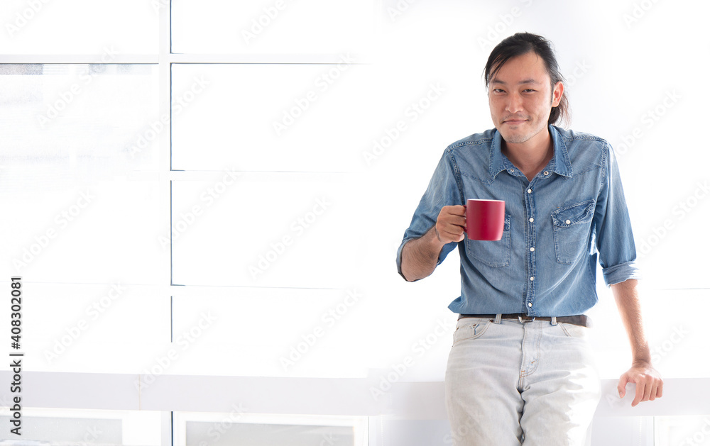 Obraz premium asian guy smile with red cup of hot coffee in the morning