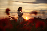 Silhouettes of a girl on a background of sunset in a field of red flowers
