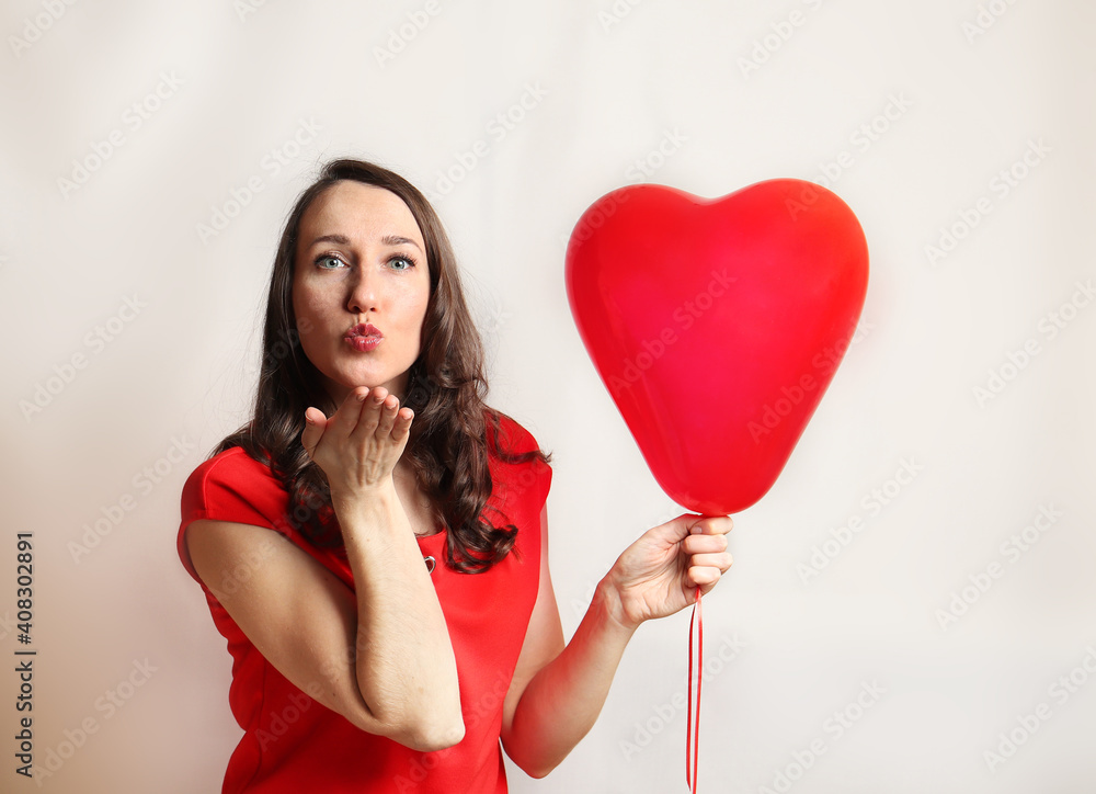 Beautiful woman sends air kiss with red balloon heart shape over white background. Beautiful happy young woman on a birthday holiday, Valentine's day, Mothers day. Close-up Beautiful woman sends air kiss with red balloon heart shape over white background. Beautiful happy young woman on a birthday holiday, Valentine's day, Mothers day. Close-up