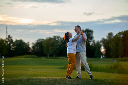 Happy couple dancing outdoors. Mature man and woman on the green field.