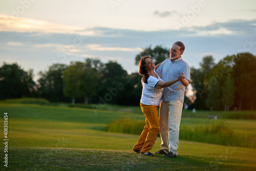 Mature couple dancing tango outdoors. Man and woman on the green field.