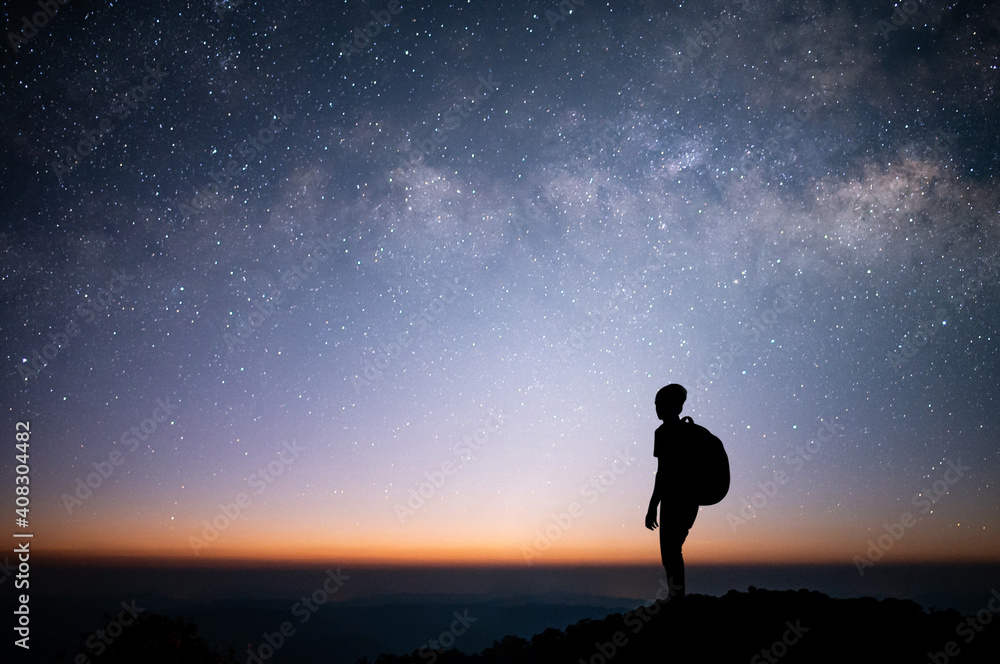 Silhouette of young traveler watched the star and milky way on top of the mountain alone in the morning before sunrise. He is happy to be with herself and stay with nature at twilight time.