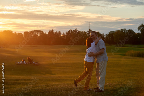 Happy couple hugging during sunset. Green summer field background.