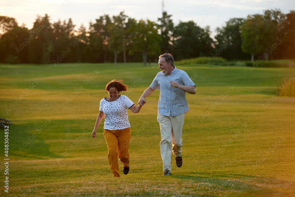 Happy laughing couple running on the grass. Man and woman holding hands. Green field background. Happy laughing couple running on the grass. Man and woman holding hands. Green field background.