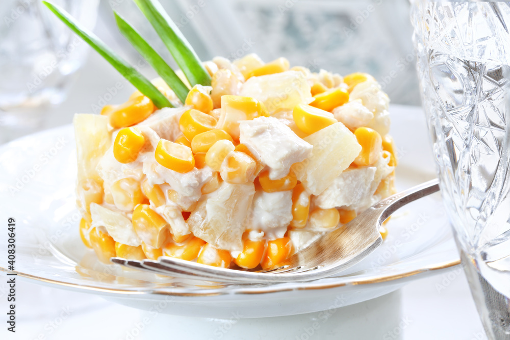 Salad with chicken, pineapple and corn with champagne on a white plate