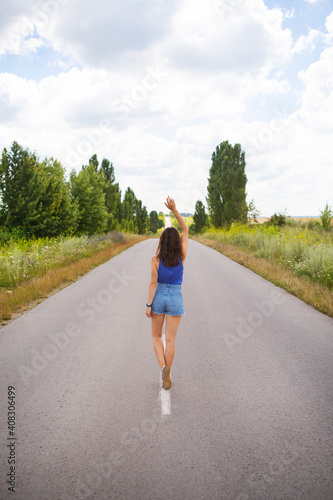 Attractive girl, stands posing, hands up in the middle of an asphalt road near the field, copies space for content
