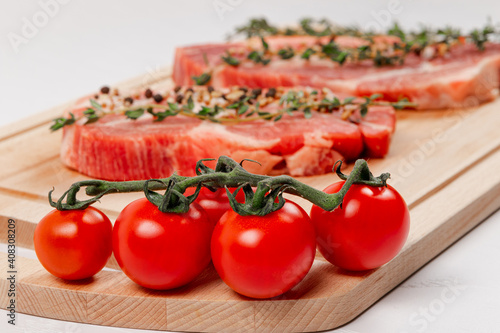 fresh chopped raw pork steaks with spices, tomatoes and thyme on a cutting kitchen board on a white wooden table