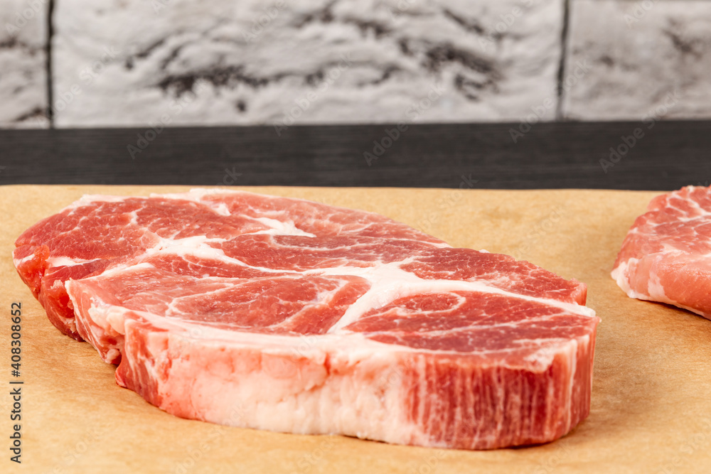fresh raw marbled meat pork steak on brown parchment paper on black table against gray brick wall background