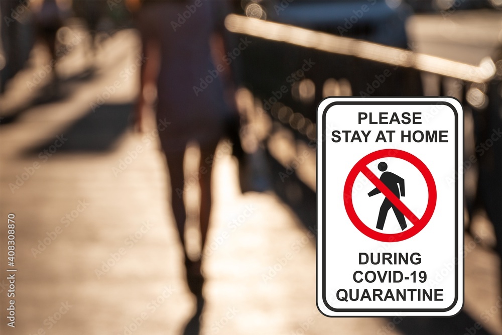 ''Please stay at home during COVID-19 quarantine'' road sign against a defocused walking girl in the city