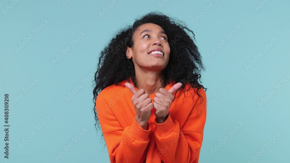 Back rear view young pretty african american woman with curly hair 20s years old in orange sweatshirt turn around camera showing thumbs up like gesture isolated on pastel blue color background studio Back rear view young pretty african american woman with curly hair 20s years old in orange sweatshirt turn around camera showing thumbs up like gesture isolated on pastel blue color background studio