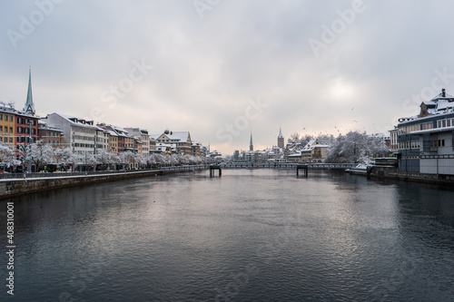 Waterside view of snow covered Zurich city Switzerland from a bridge crossing the Limmat river winter time cloudy day