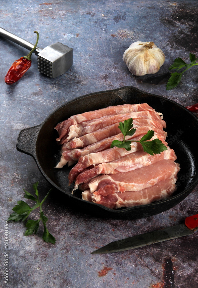Raw pork meat slices with spices and herbs in a black pan. Black background. Top view space for text Raw pork meat slices with spices and herbs in a black pan. Black background. Top view space for text