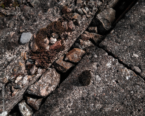 Surface of concrete and crushed stone texture with gap, moss and small pebbles. 