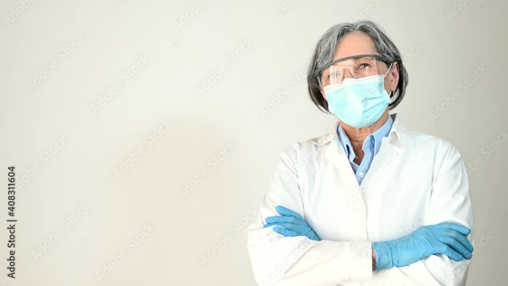 Confident senior female doctor in white professional coat, wearing protective mask, goggles and gloves crossed her arms and looking at the camera, isolated. Fight against coronavirus and viral disease Confident senior female doctor in white professional coat, wearing protective mask, goggles and gloves crossed her arms and looking at the camera, isolated. Fight against coronavirus and viral disease