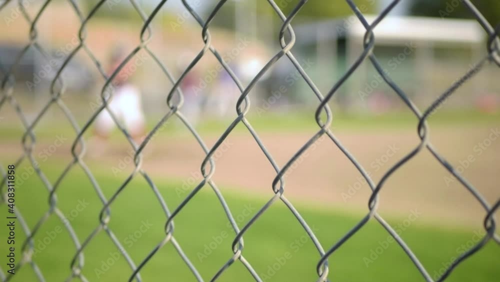 Little league player swinging during practice, defocused behind fence Little league player swinging during practice, defocused behind fence