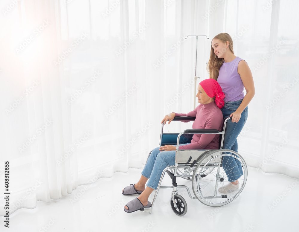 A cancer-stricken mother sits in a wheelchair looking at the evening sun, with her daughter visiting as a wheelchair in a hospital ward. A cancer-stricken mother sits in a wheelchair looking at the evening sun, with her daughter visiting as a wheelchair in a hospital ward.
