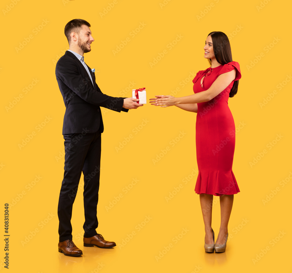 Man Giving Gift To Girlfriend Standing On Yellow Studio Background Man Giving Gift To Girlfriend Standing On Yellow Studio Background