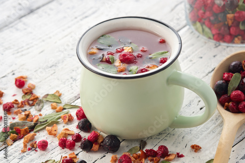 Cup of healthy fruit tea with apples, orange, red and black currant berries. Wooden spoon of dry ingredients for making tea.