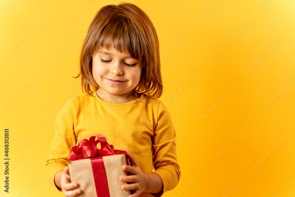 Kid girl on a yellow background receives a gift, a box with a red bow, a surprise Kid girl on a yellow background receives a gift, a box with a red bow, a surprise