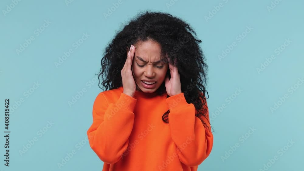 Sick ill young african american woman 20s years old in orange sweatshirt put hands on head rub temples having headache migraine feel bad seedy isolated on pastel blue color background studio portrait Sick ill young african american woman 20s years old in orange sweatshirt put hands on head rub temples having headache migraine feel bad seedy isolated on pastel blue color background studio portrait
