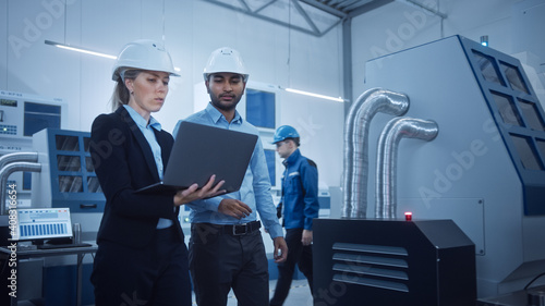 Female Chief Engineer and Male Project Manager Walk Through Modern Factory, Talking and Planning Optimization of the Production. Industrial Facility: Professionals Working on CNC Machinery, robot arm