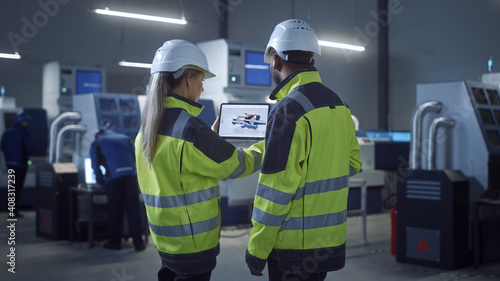 Industry 4.0 Factory: Chief Engineer and Project Supervisor in Safety Vests and Hard Hats, Talk, Use Digital Tablet, Screen Shows 3D Concept of New Jet Engine. Industrial Workshop with Machinery.