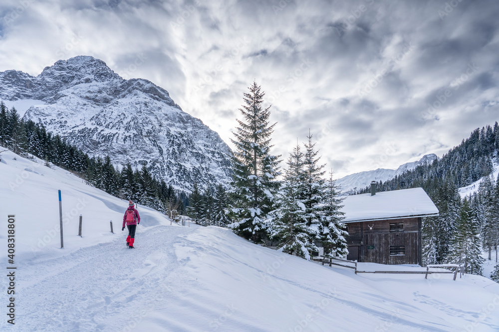 active senior woman hiking in the snowy mountains of Kleinwalsertal, Vorarlberg, Austria, near village of Baad, below the summit of Widderstein  
