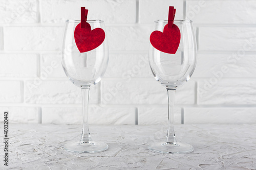on the white textured surface there are two wine-empty glasses with red hearts, in the background a white brick wall photo