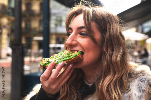 Young caucasian woman having breakfast at a terrace eating an avocado toast.