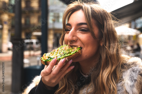 Young caucasian woman having breakfast at a terrace eating an avocado toast.