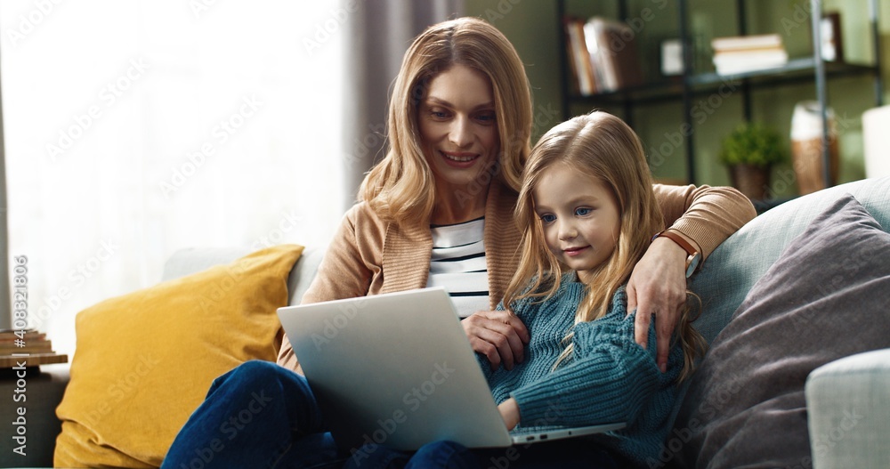 Happy mom with little daughter sitting hugging on sofa at home and watching cartoons online using laptop. Happy mom with little daughter sitting hugging on sofa at home and watching cartoons online using laptop.
