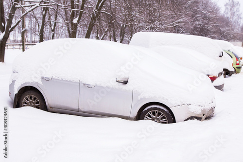 Many cars on parking under snow in snowbank after snowfall and blizzard