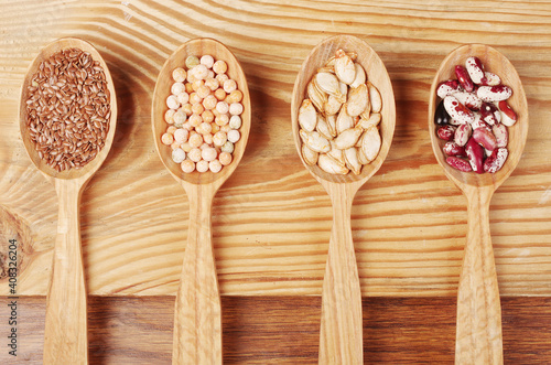 Four wooden spoons with various seeds of wheat, peas, pumpkin, beans.