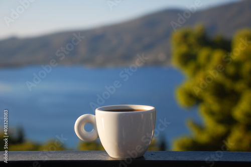 A cup of hot coffee on the background of the sea, hills and blue sky on the Greek island of Poros. photo