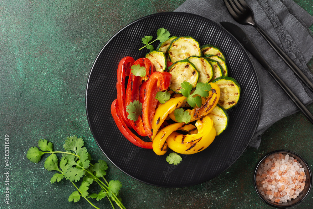 Grilled vegetables pieces of zucchini, red and yellow pepper and bouquet of cilantro on plate, salad on bbq grill rack over charcoal. Top view. Barbecue concept Grilled vegetables pieces of zucchini, red and yellow pepper and bouquet of cilantro on plate, salad on bbq grill rack over charcoal. Top view. Barbecue concept