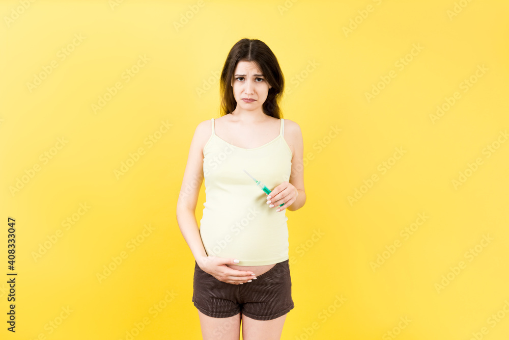 pregnant woman holding a syringe against her belly at colorful background with copy space. Injection during pregnancy concept pregnant woman holding a syringe against her belly at colorful background with copy space. Injection during pregnancy concept