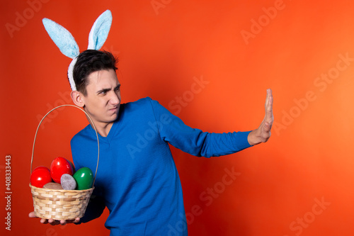 Handsome young guy holding a basket with eggs in his hands. Easter traditions. Orange background.