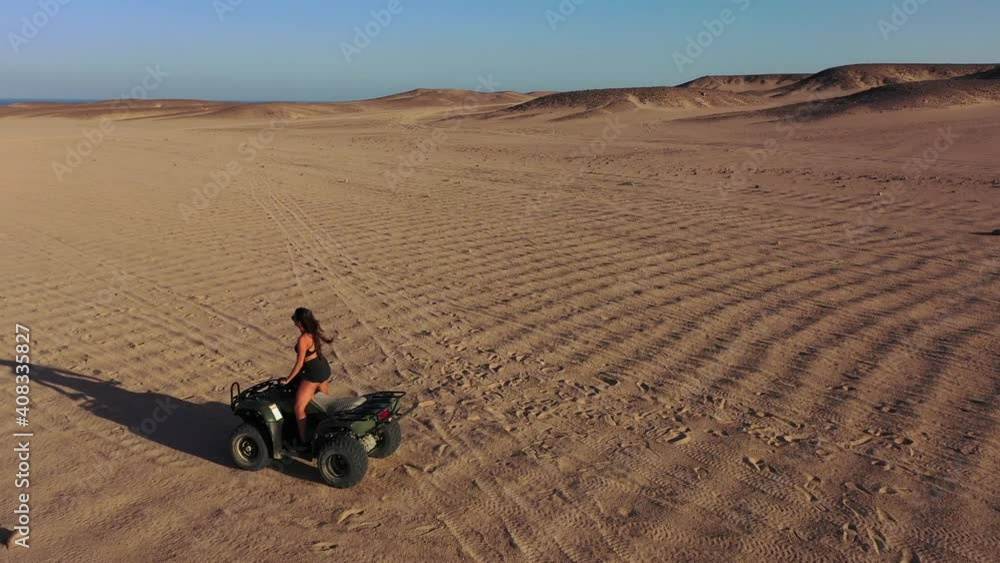 Aerial side reveal shot of girl standing up on quad bike in desert