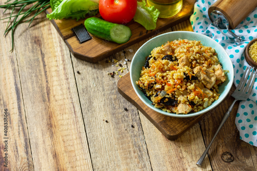 Bulgur with turkey and prunes is served with fresh vegetable on a rustic table. Copy space. Bulgur with turkey and prunes is served with fresh vegetable on a rustic table. Copy space.