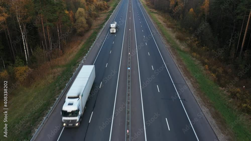 Cars and trucks are driving on empty highway along autumn forest Cars and trucks are driving on empty highway along autumn forest