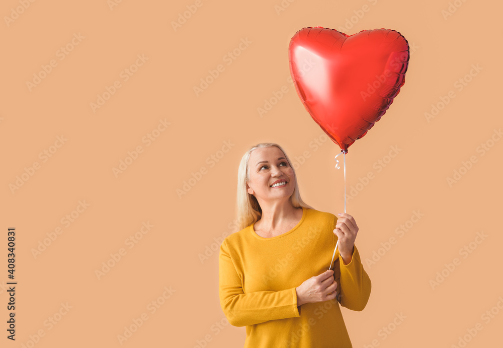 Mature woman with red heart-shaped balloon on color background Mature woman with red heart-shaped balloon on color background