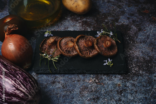 Top view of mushroom on black granite slab with potato, tomato, onion, oil and eggplant.